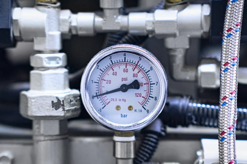 Manômetro com escala em bar e em psi, de −1 a 9 bar, instalado entre conexões roscadas de aço, com uma mangueira de malha trançada ao lado