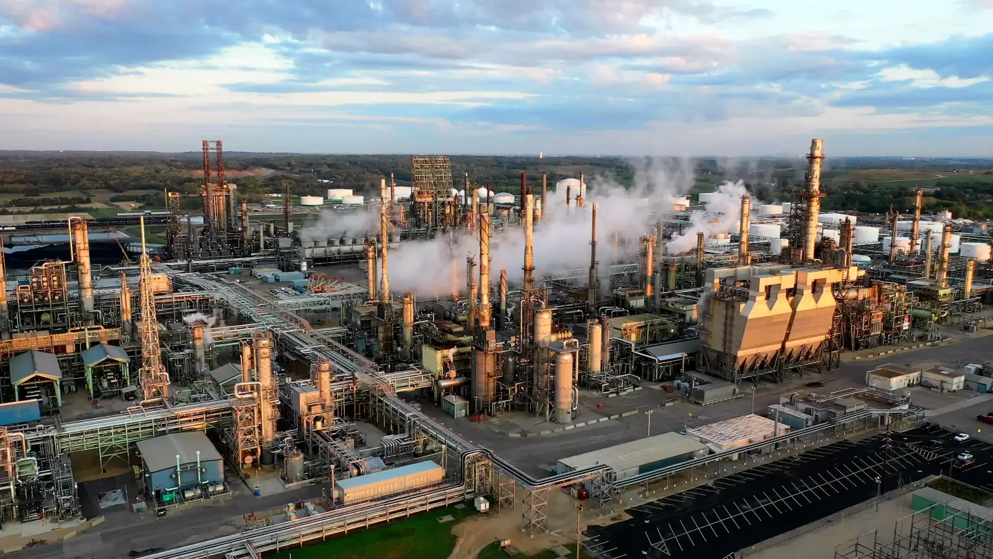 Refinaria vista do alto ao entardecer, com colunas de processo, tubulações e vapor