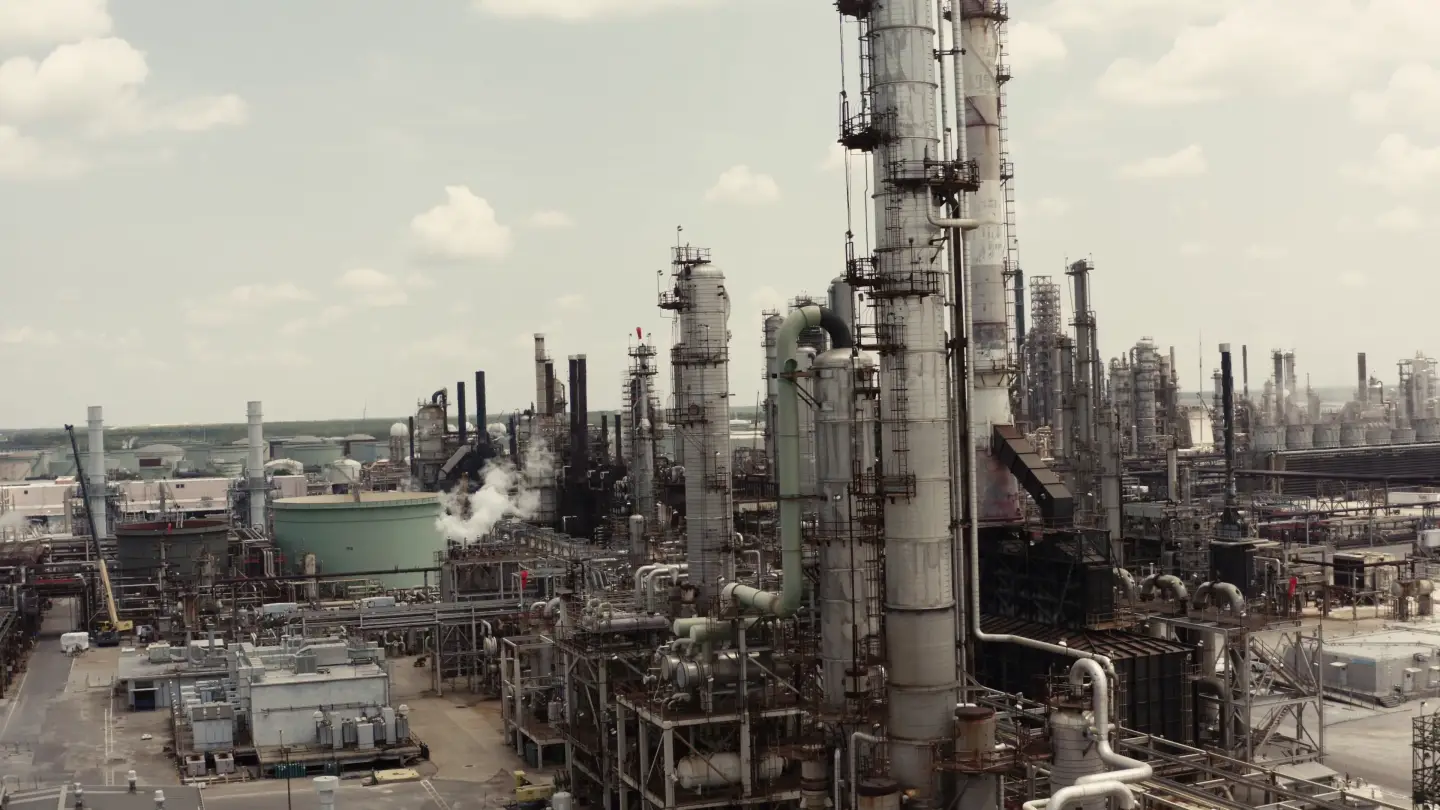 Vista de drone das colunas de destilação de uma refinaria, com plataformas no topo, escadas, linhas de processo e vapor saindo da unidade